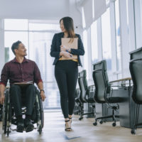 2 office workers walking side by side, 1 in wheelchair