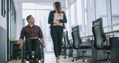 2 office workers walking side by side, 1 in wheelchair