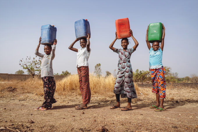 Four young girls,in a rural African village, transporting clean water in heavy plastic cans to help their community.