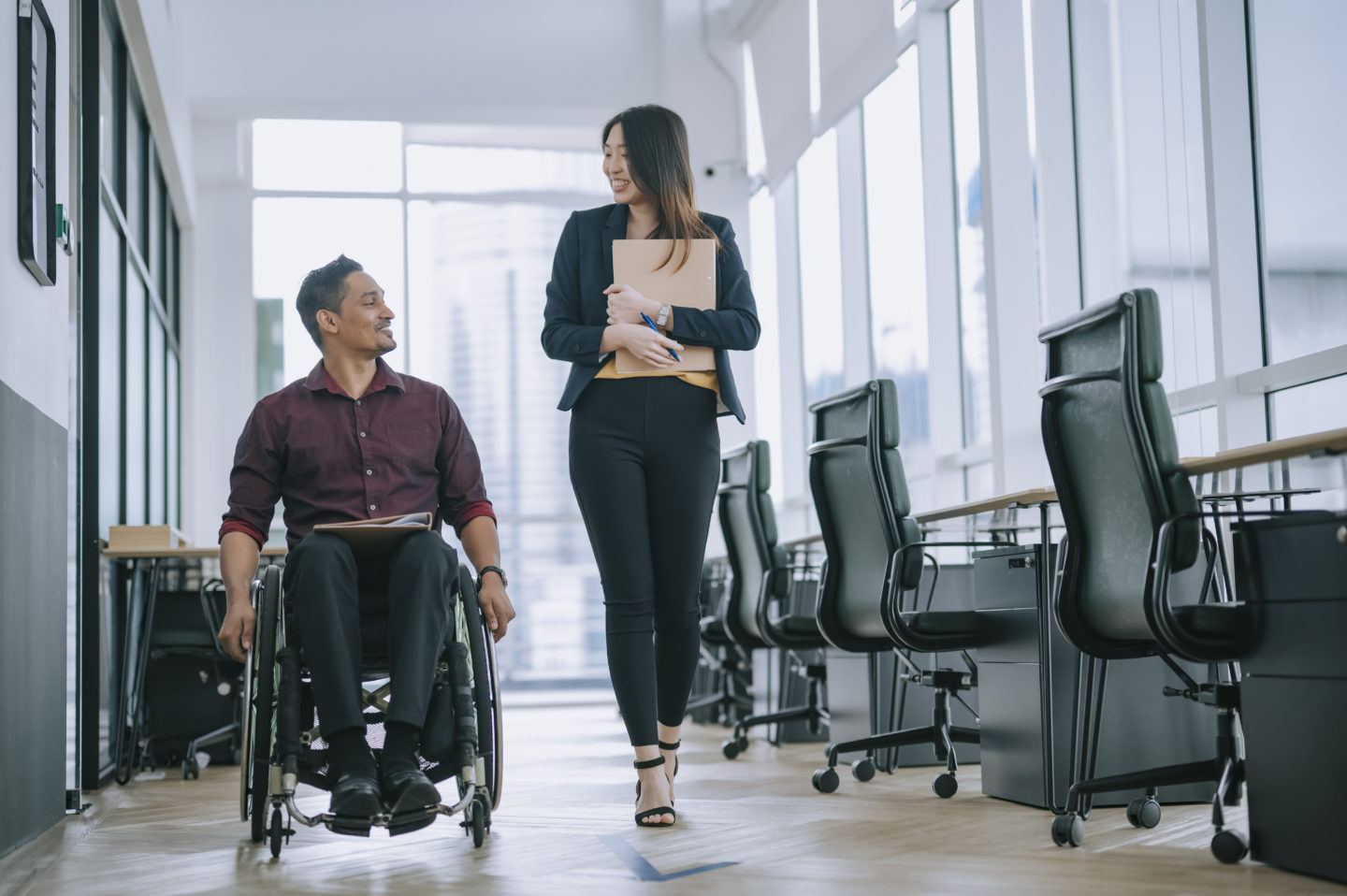2 office workers walking side by side, 1 in wheelchair