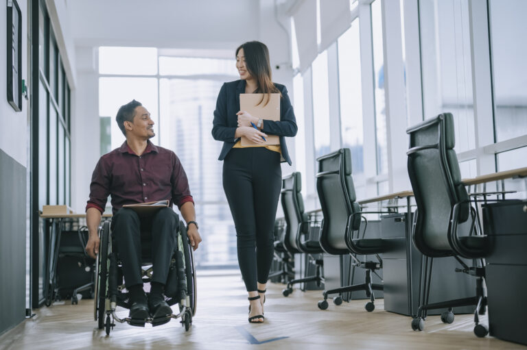 2 office workers walking side by side, 1 in wheelchair
