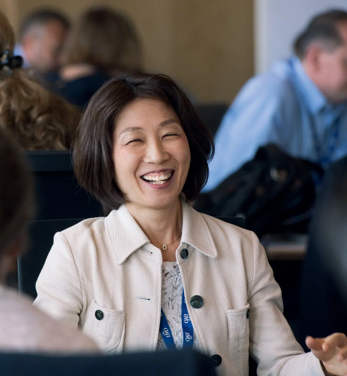 Woman smiling and participating in an IMD executive education discussion session with other attendees in the background. - IMD Business School