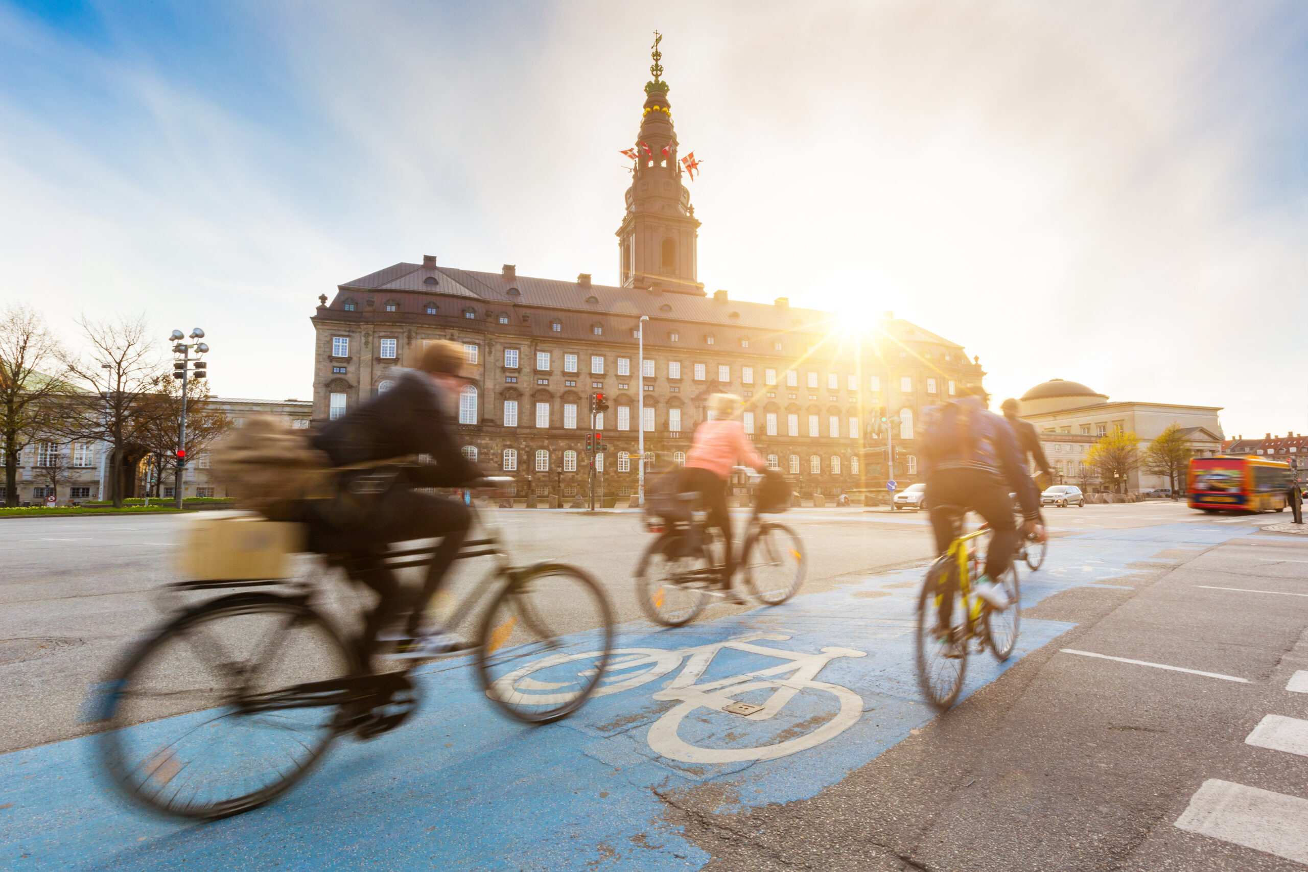 Blurred people going by bike in Copenhagen, with Christiansborg palace on background. Many persons prefer biking instead of taking car or bus to move around the city. Urban lifestyle concept. - IMD Business School