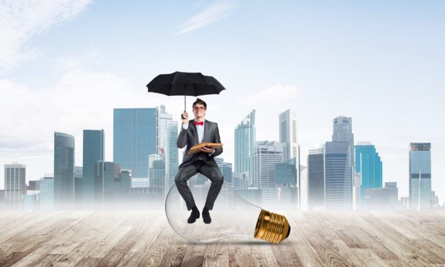 Man sitting on a light bulb, holding an umbrella. A city in a background - IMD Business School