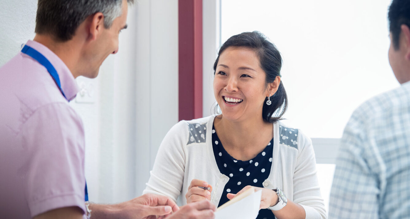 Smiling woman speaking with two colleagues during an executive education discussion in a bright classroom setting. - IMD Business School