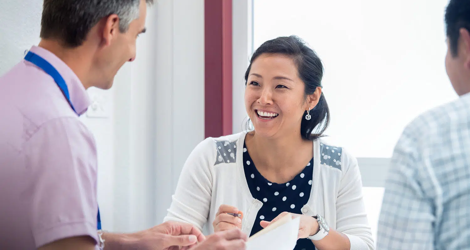 Smiling woman speaking with two colleagues during an executive education discussion in a bright classroom setting. - IMD Business School