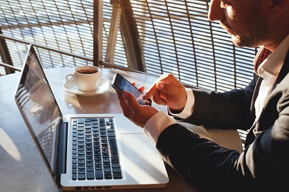 Man looking at a smartphone and sitting in front of a laptop - IMD Business School