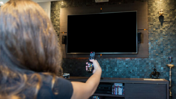 Young woman switching TV channels with remote control,