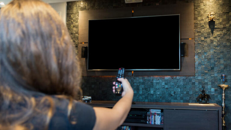 Young woman switching TV channels with remote control,