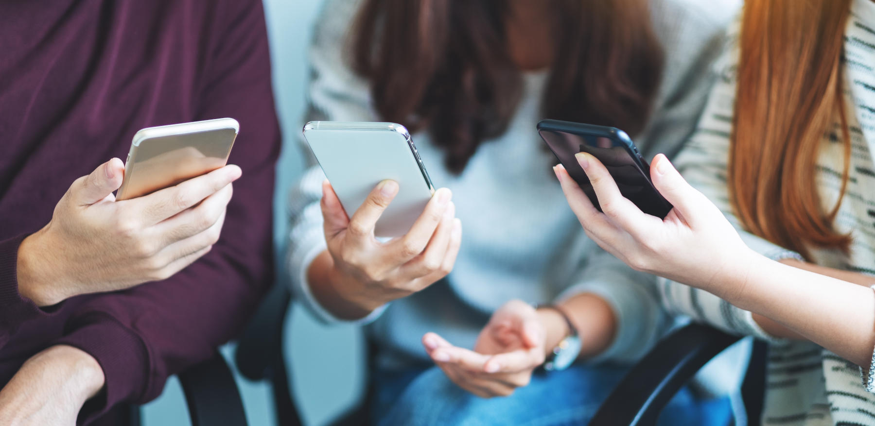 Group of young people using and looking at mobile phone while sitting together