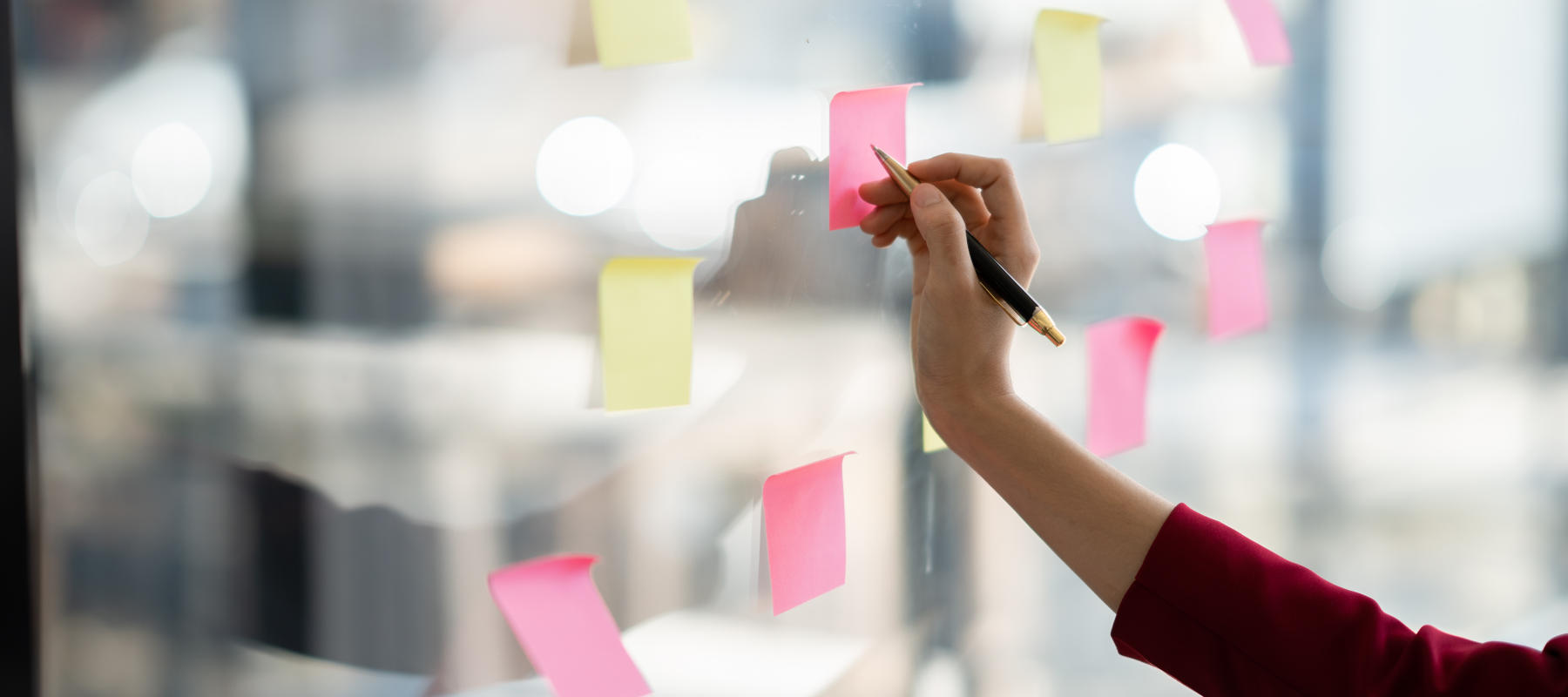 Close up view of business woman writing idea or task on post it sticky notes on glass wall, prepare for the meeting time.