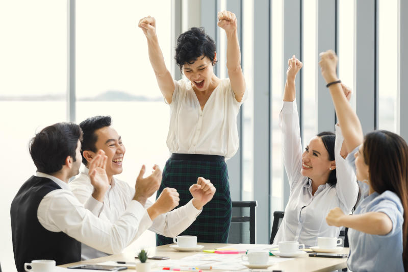Group of five diverse businessmen two men and three women at meeting desk The woman feels excited and the team congrats and cheer her up Group of five diverse businessmen two men and three women at meeting desk The woman feels excited and the team congrats and cheer her up