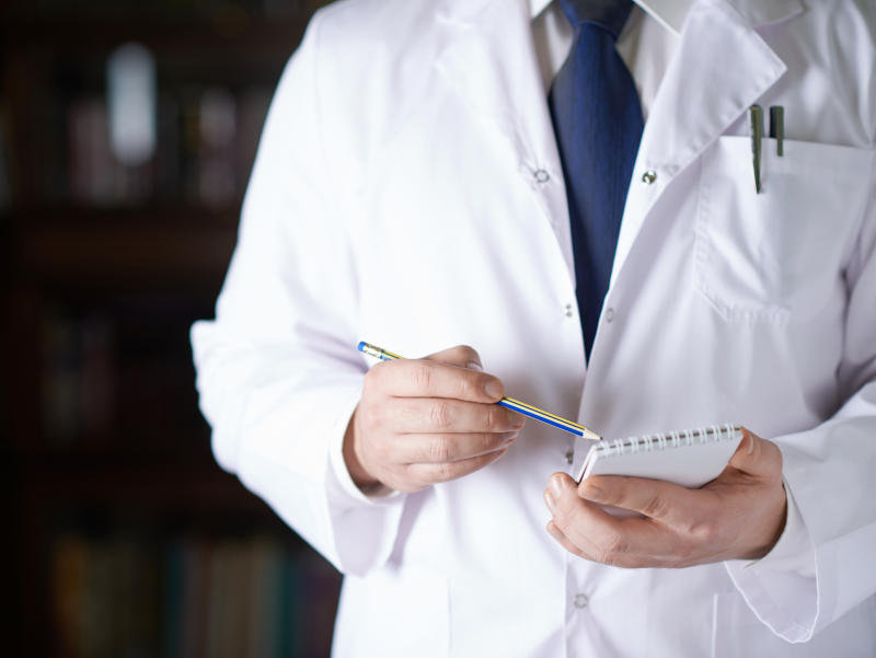 Close-up fragment of a man in a white doctor's coat writing down something in a notebook with a pencil, shallow depth of field composition