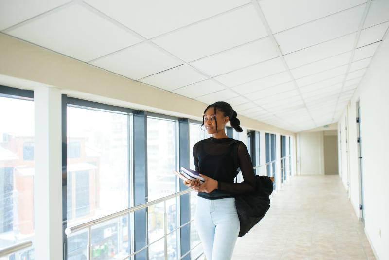Pretty female student with backpack and paperwork at classroom of university