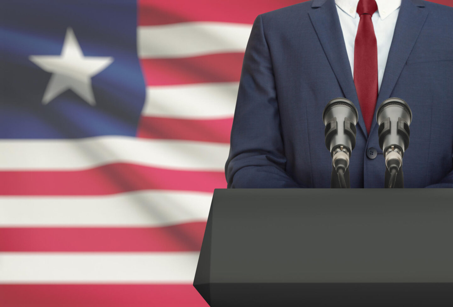 Businessman or politician making speech from behind the pulpit with national flag on background - Liberia