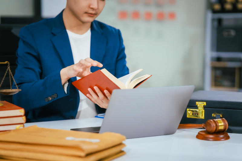 A male lawyer works diligently at his desk in a law office and courtroom reviewing documents He provides online legal consultations assists businesses and ensures justice through professional