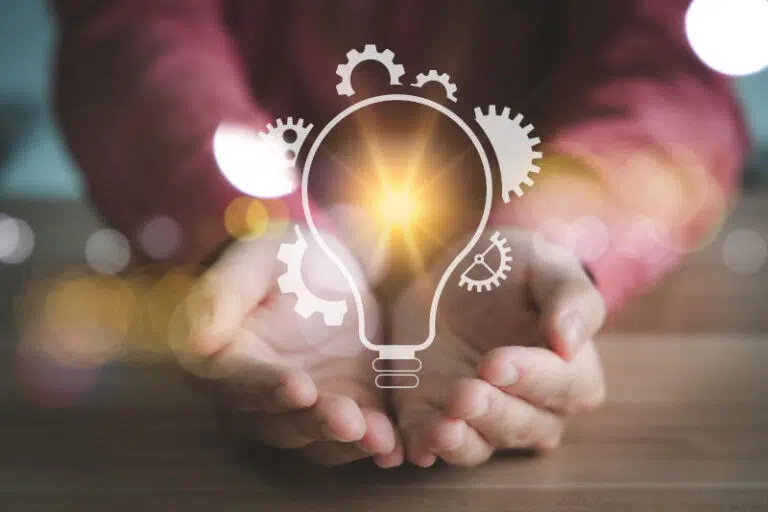People holding shining light bulb with gear icons Concept of creativity innovation and technology - IMD Business School