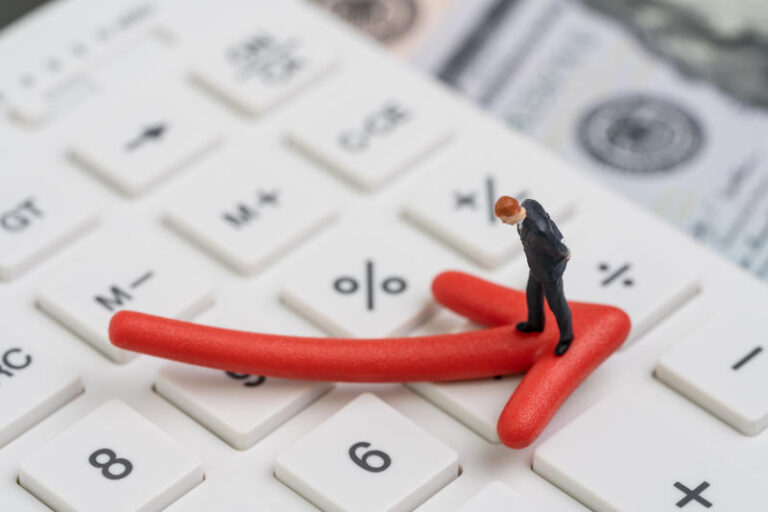 Economic recession bear stock market or financial crisis concept miniature businessman standing on red pointing down arrow on white calculator with background of US dollar banknote money