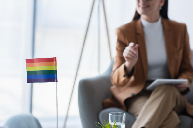 small lgbt flag near cropped psychologist with digital tablet on blurred background