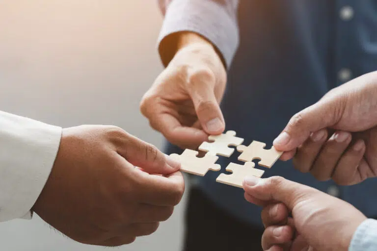 business people team holds in hand a jigsaw or puzzle pieces in the office for concept of troubleshooting teamwork Unity and partnership success and strategy concept - IMD Business School
