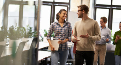 Two young diverse business people male and female coworkers talking discussing project and smiling while walking down the modern office