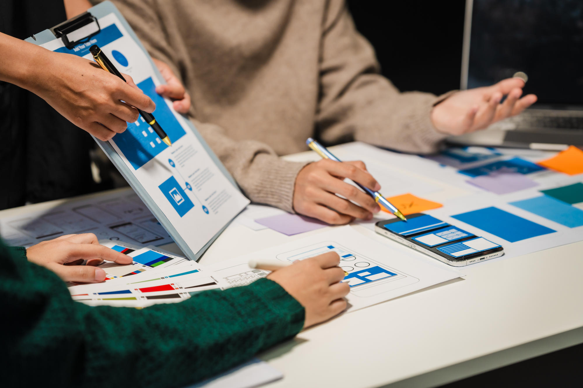 Close-up of hands working on UXUI design at a desk Papers with wireframes prototypes and mockups detail user flows personas and AB testing ensuring usability and responsive design