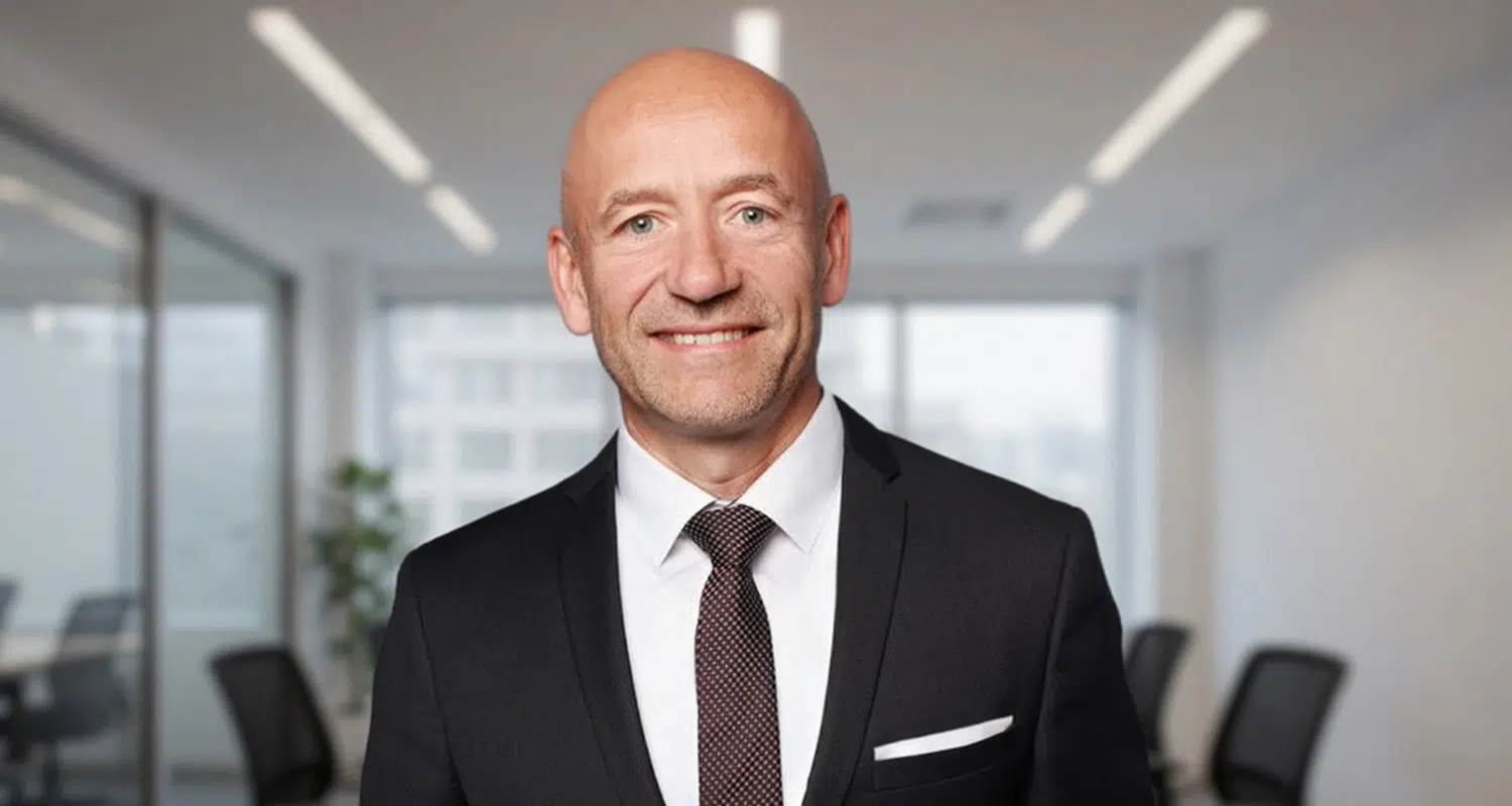 Portrait of Christoph Heidler, an IMD participant, standing in a modern office wearing a dark suit and smiling at the camera. - IMD Business School