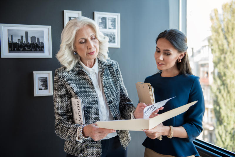Serious stylish aged female is standing with her employee