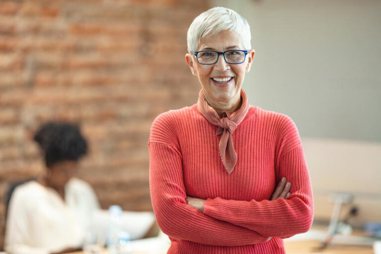 Close-up portrait of mature business woman standing at office Pretty older business woman successful confidence with arms crossed in financial building Mature female in office with team