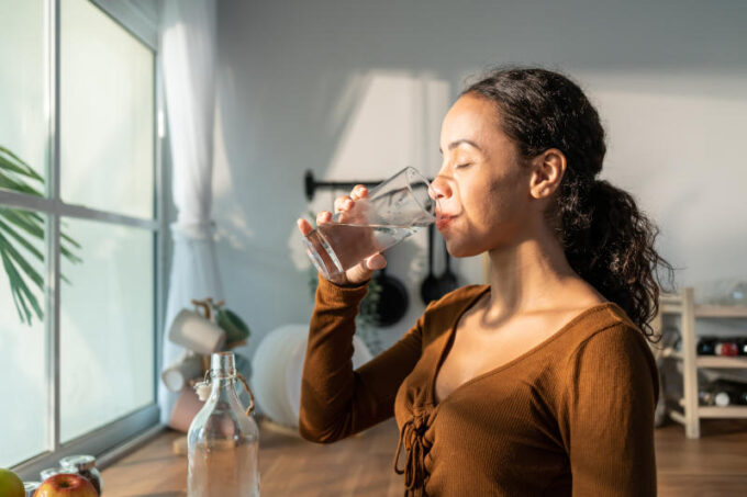 Young beautiful Latino woman holding clean water into glass in k
