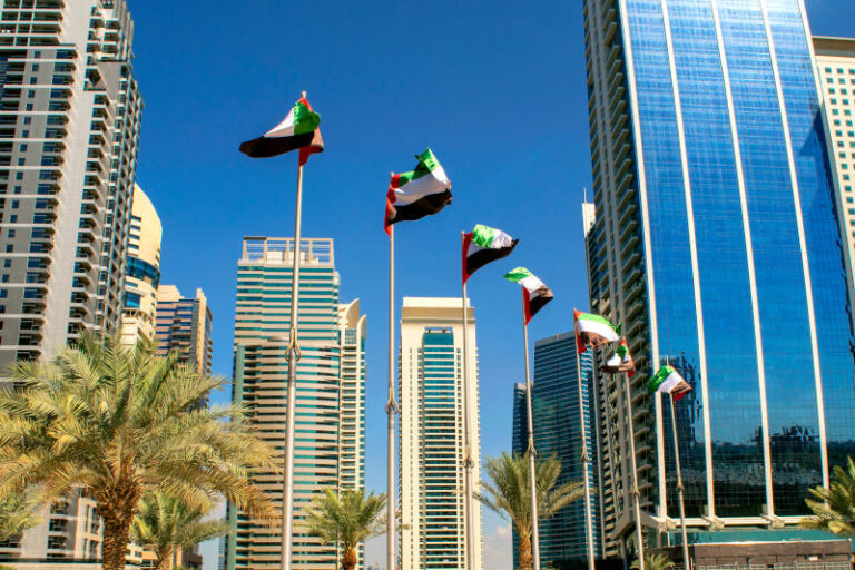 View of Dubai buildings with UAE flags United Arab Emirates flags waving on blue sky background Independence day UAE flags on street Flag day