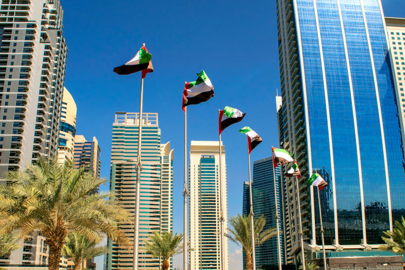 View of Dubai buildings with UAE flags United Arab Emirates flags waving on blue sky background Independence day UAE flags on street Flag day
