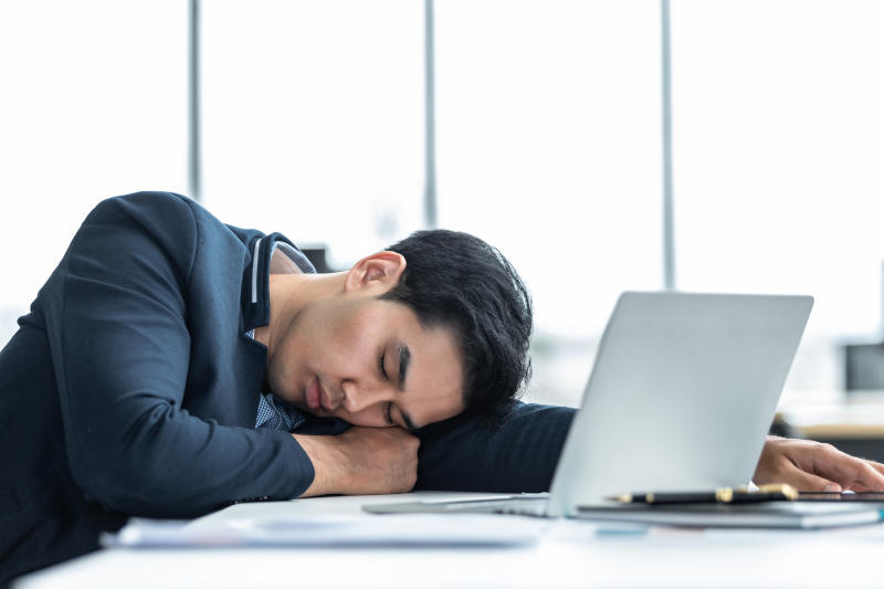 Asian young businessman worked late and fell asleep on laptop computer In the office room background