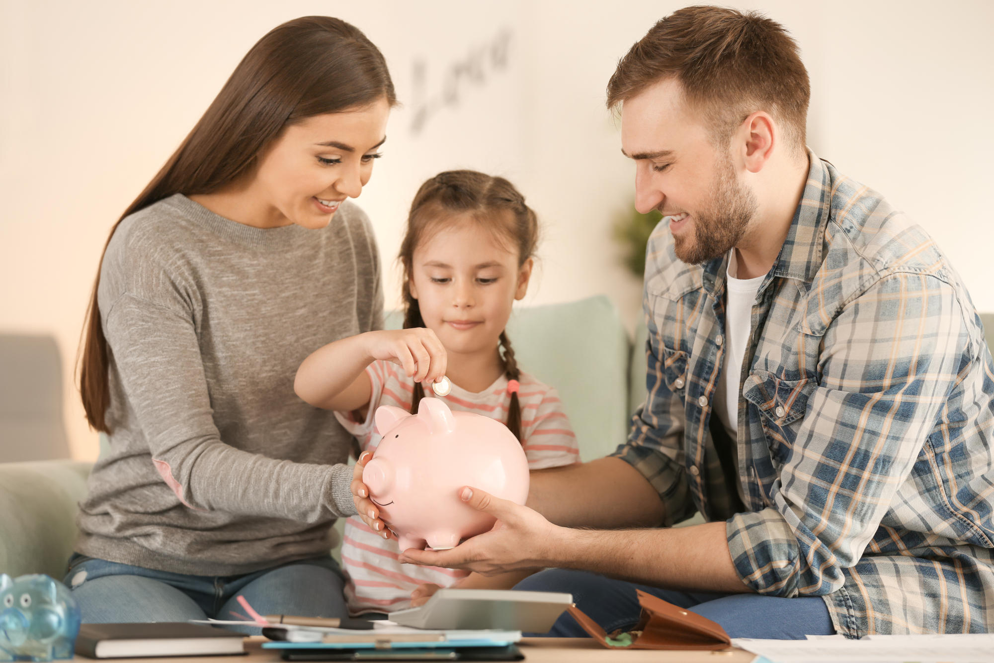 Little girl with her parents sitting on sofa and putting coin in Little girl with her parents sitting on sofa and putting coin in