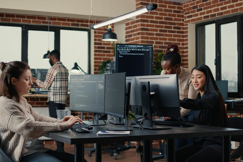 Software engineer typing source code on computer keyboard while colleagues sit down at desk