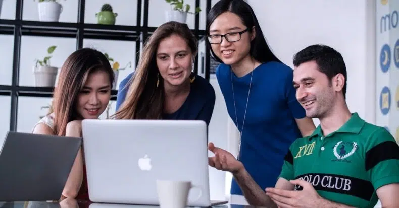 four people standing behind a laptop, working together - IMD Business School