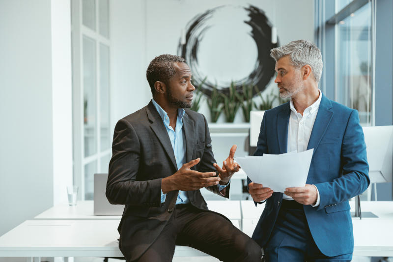 Two businessmen talking about deal sitting in meeting room in modern office