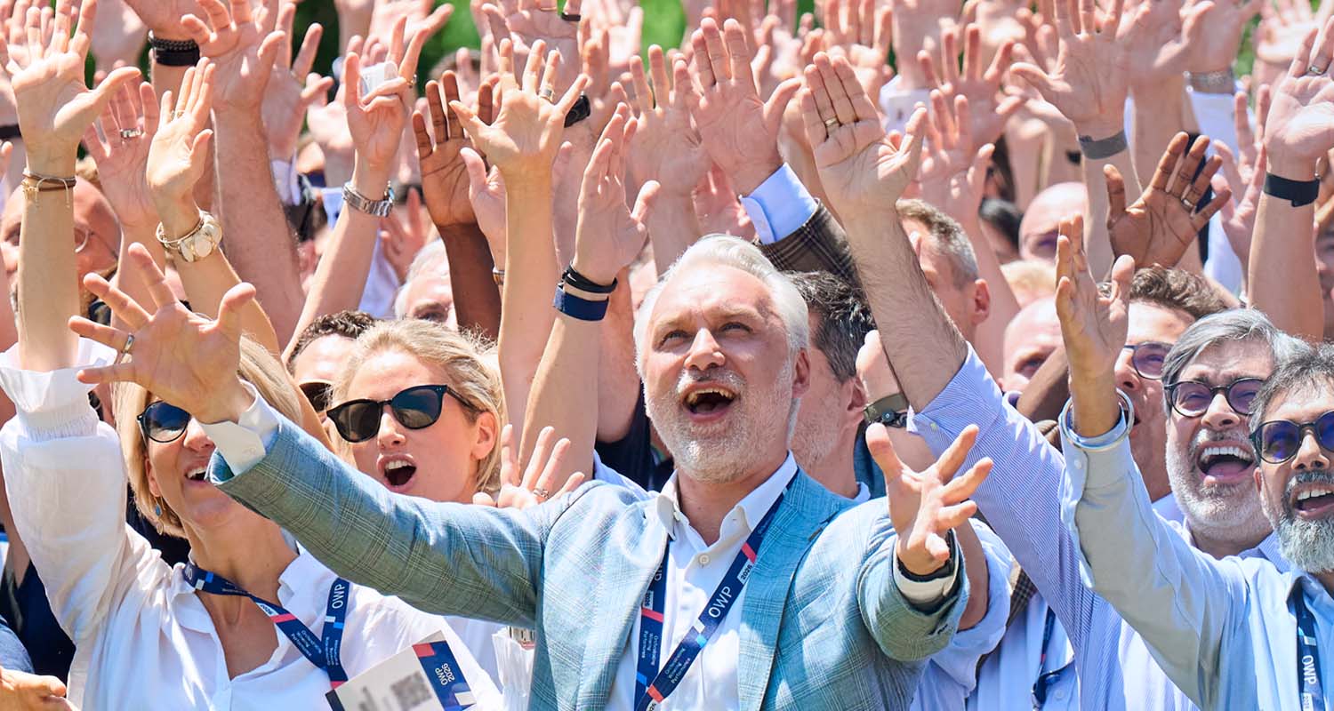 Participants attending IMD's Orchestrating Winning Performance (OWP) program gathered outdoors with their hands raised. - IMD Business School