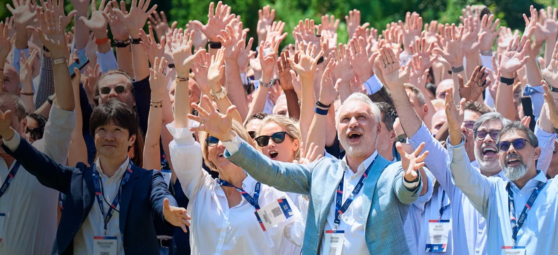 Participants attending IMD's Orchestrating Winning Performance (OWP) program gathered outdoors with their hands raised. - IMD Business School