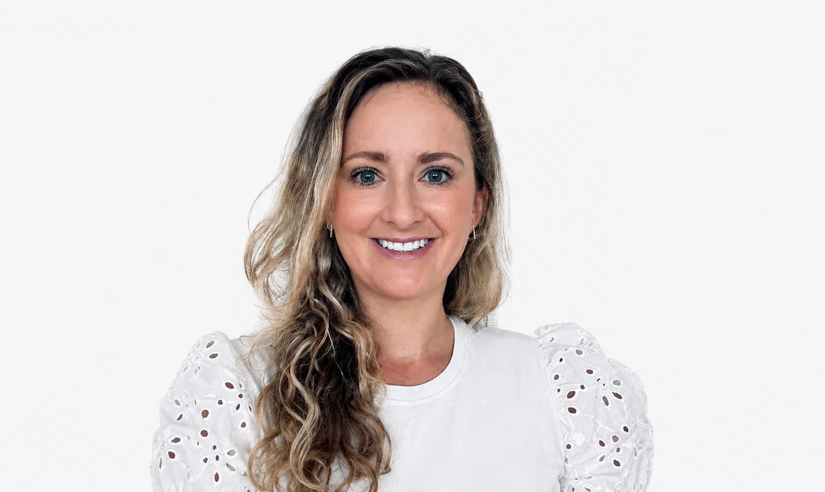 Smiling woman with shoulder-length wavy blonde hair and blue eyes, wearing a white top with eyelet sleeves, facing the camera - IMD Business School