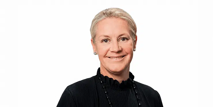 Portrait of a smiling middle-aged woman with short gray hair, wearing a black top and necklace. - IMD Business School