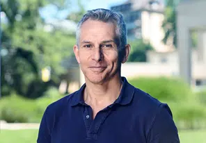Portrait of a middle-aged man in a navy polo shirt outdoors, with a green park background and a subtle smile. - IMD Business School