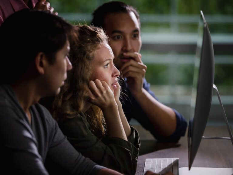 Selective focus on Caucasian beautiful worry face of woman getting bad news of failure project while looking together at computers screen with multiethnic team colleagues in evening at indoor office