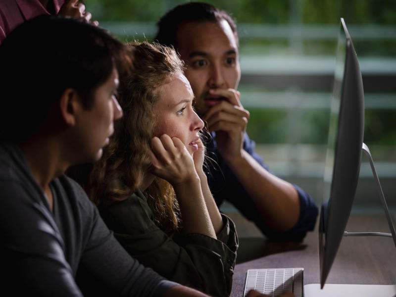 Selective focus on Caucasian beautiful worry face of woman getting bad news of failure project while looking together at computers screen with multiethnic team colleagues in evening at indoor office