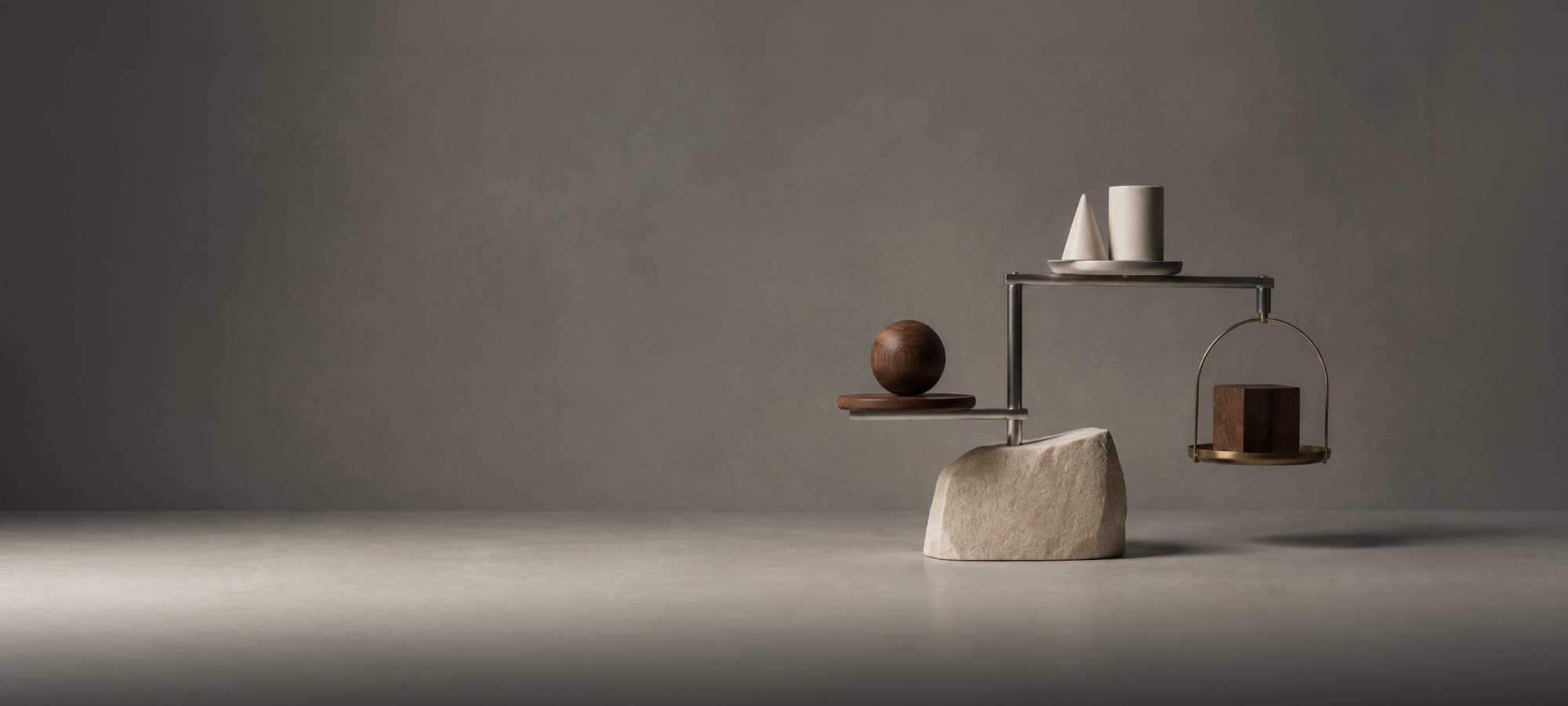 A sophisticated architectural mobile positioned in the right-hand third, composed of three distinct materials: a solid stone form, a cluster of smaller geometric objects, and a finely engineered metal framework