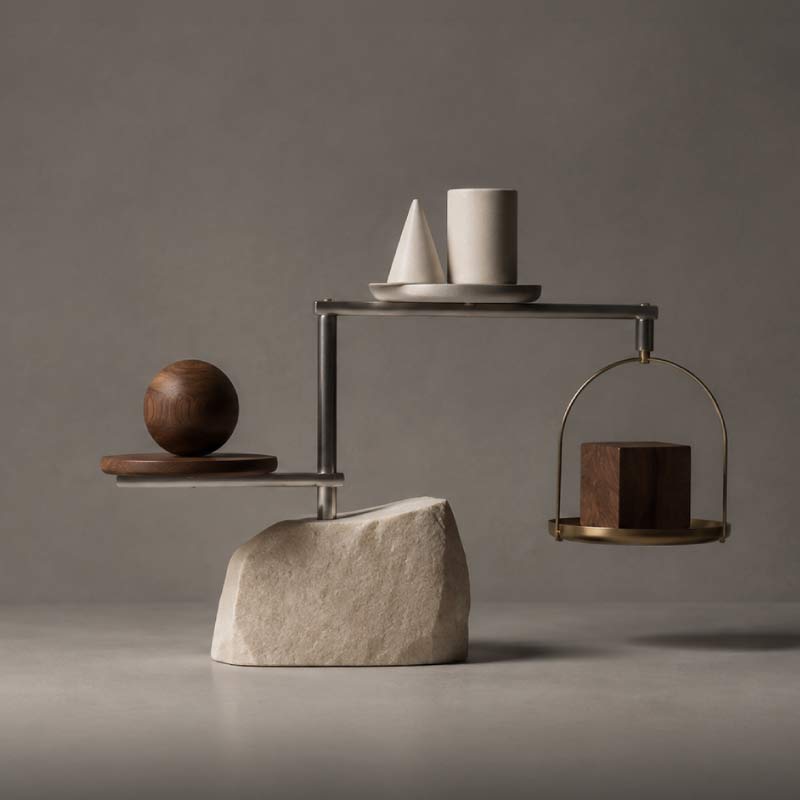 A sophisticated architectural mobile positioned in the right-hand third, composed of three distinct materials: a solid stone form, a cluster of smaller geometric objects, and a finely engineered metal framework