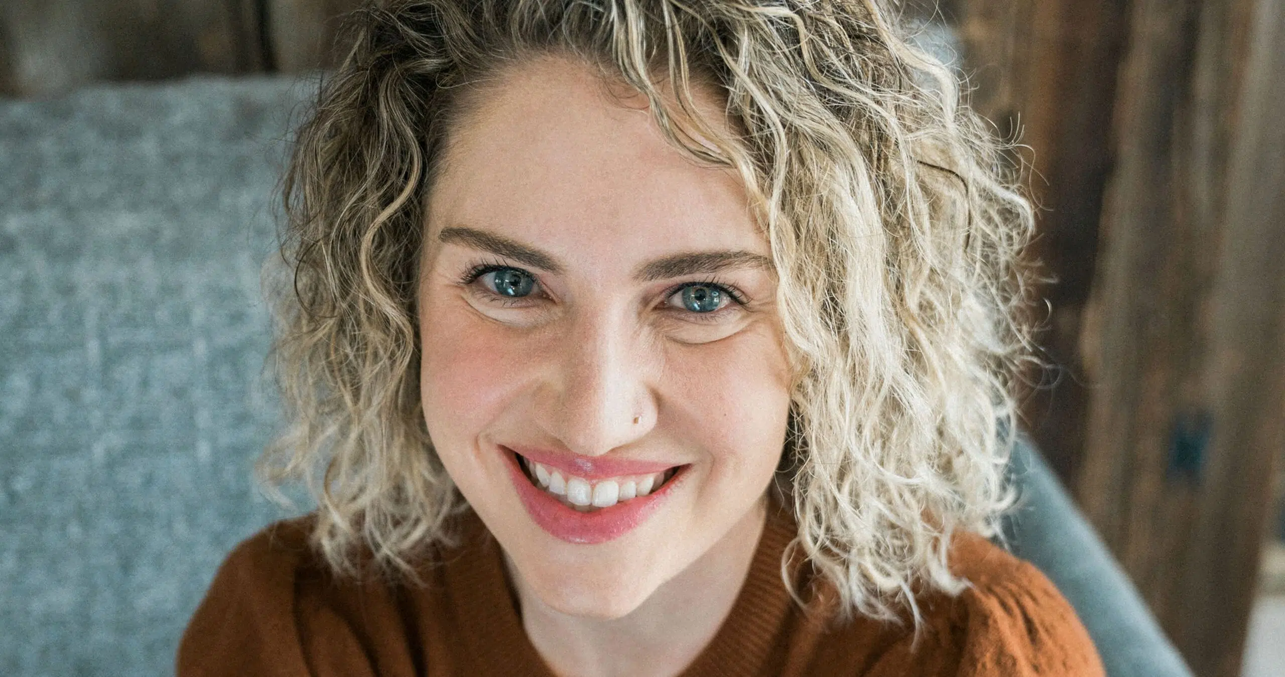 Smiling woman with curly blonde hair and blue eyes looking at the camera in a close-up portrait. - IMD Business School