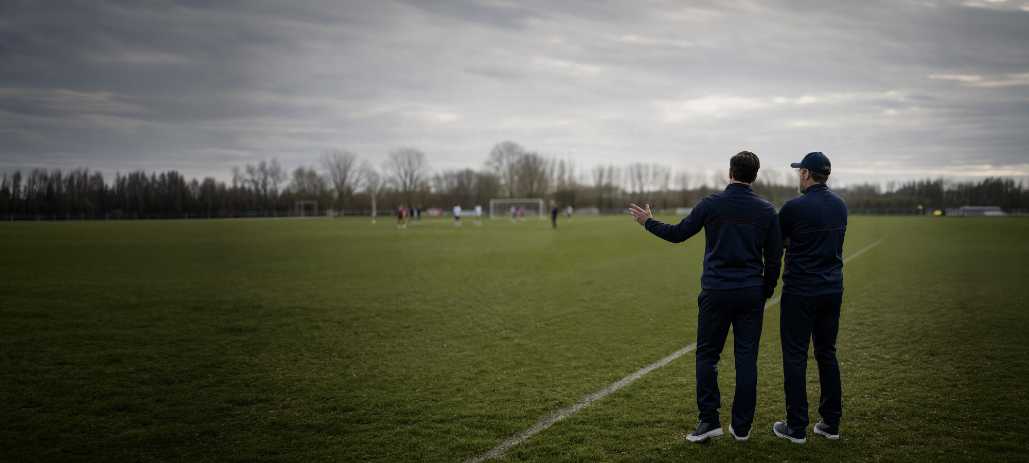 two soccer coaches standing on the side of the football field