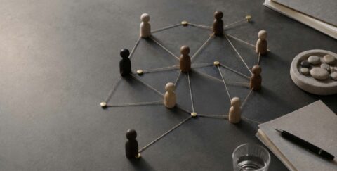 Wooden figurines connected by strings forming a social network on a desk surface, symbolizing collaboration and community.