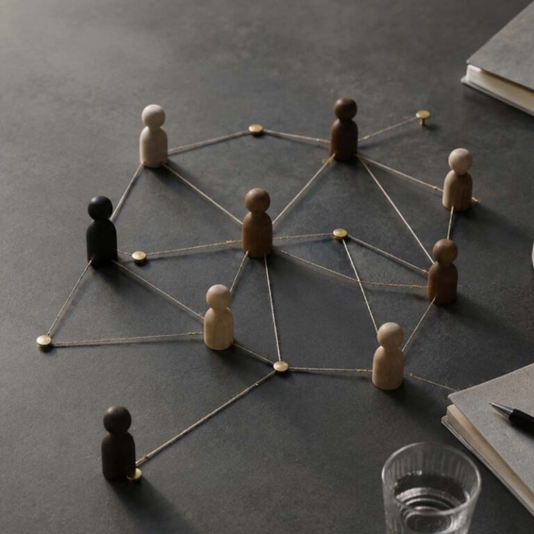 Wooden peg figures connected by strings and pins, forming a network on a desk to symbolize collaboration or social connections.
